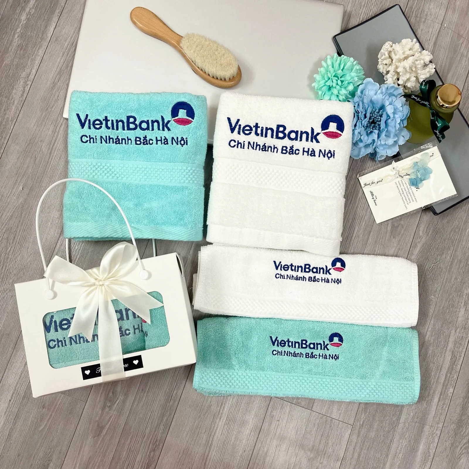 Khăn trắng và xanh thêu logo đặt cạnh hộp nơ trắng