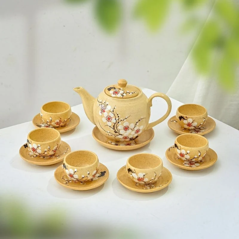 Bộ trà vẽ tay hoa trắng nền vàng bày trên bàn trắng cạnh rèm cửa