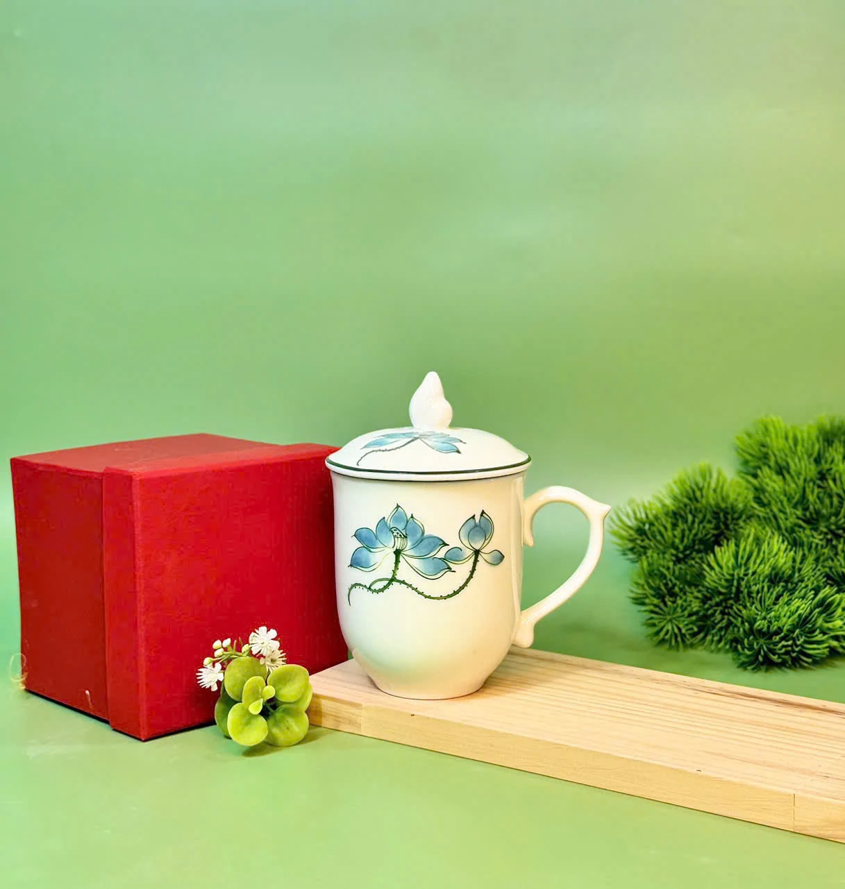 Cốc Lửa họa tiết sen xanh được bày cạnh hộp đỏ trên khối gỗ