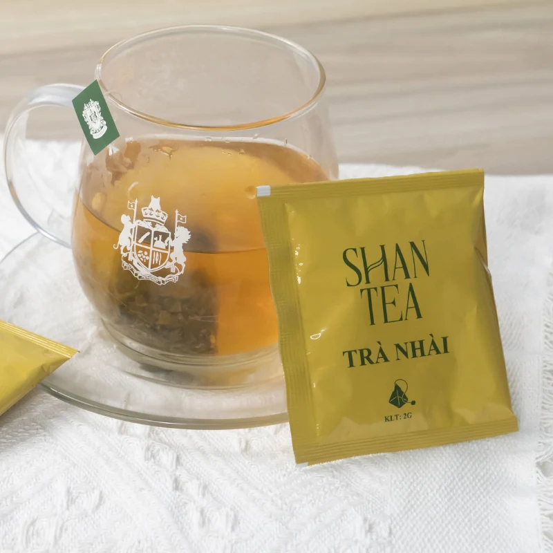 Gói trà nhài Shan Tea 2 g cạnh tách trà đang pha
