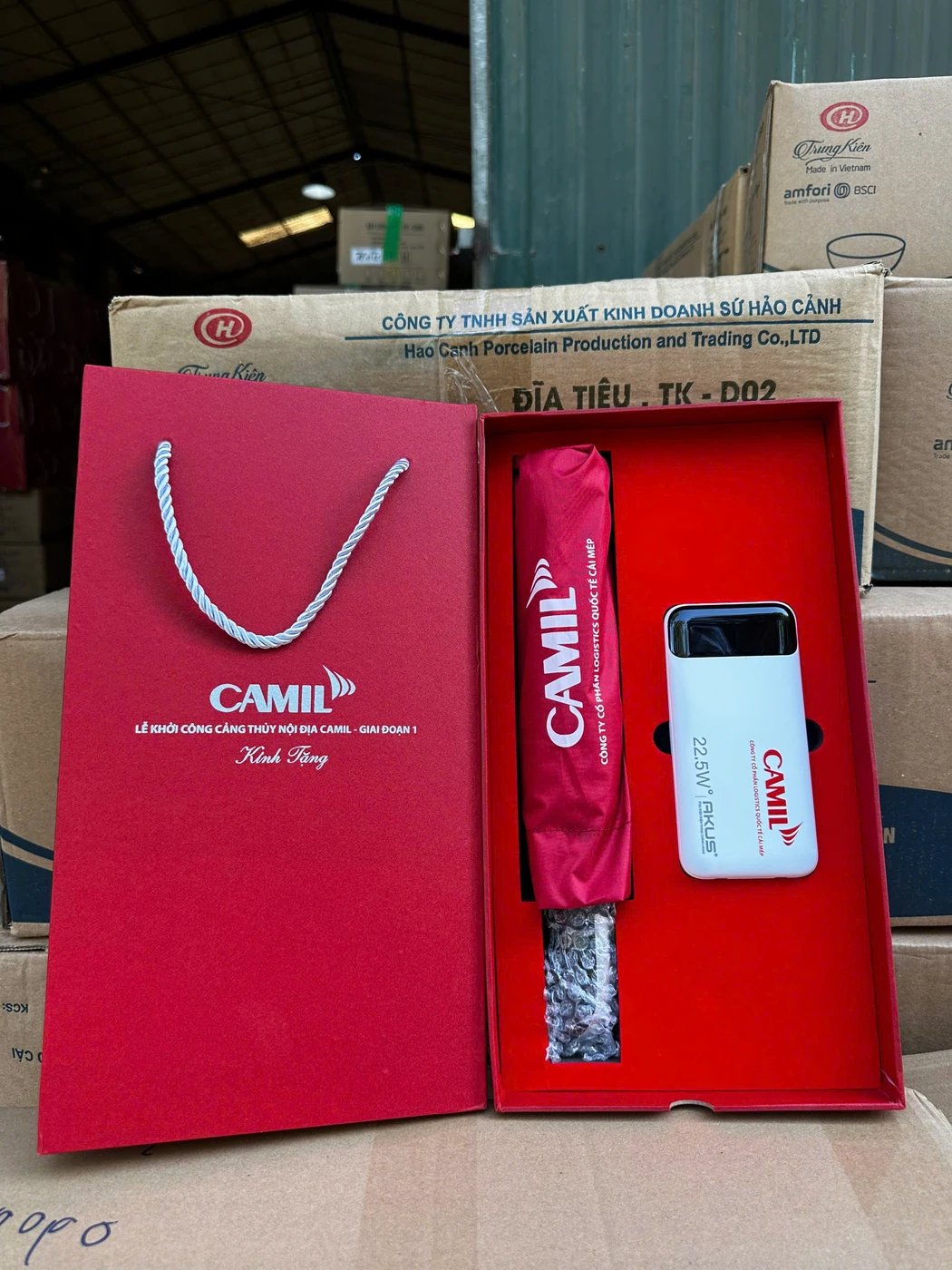 Ảnh thật bộ quà CAMIL có ô bọc đỏ, pin sạc, hộp mở và túi quai xách cùng nhận diện