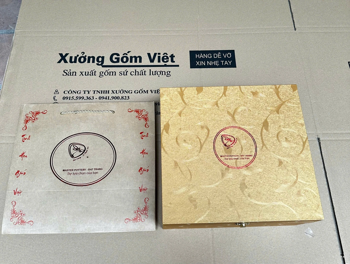 Ảnh thật một túi giấy sáng màu và hộp màu vàng có phần nhận diện, đặt trên nền nguồn Xưởng Gốm Việt
