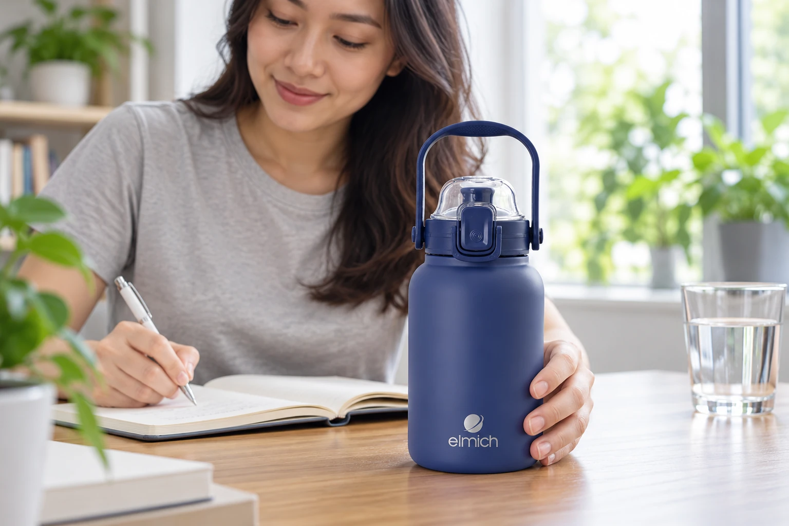 Tay đặt bình Elmich xanh đậm cạnh cuốn sổ ở bàn ghi chép