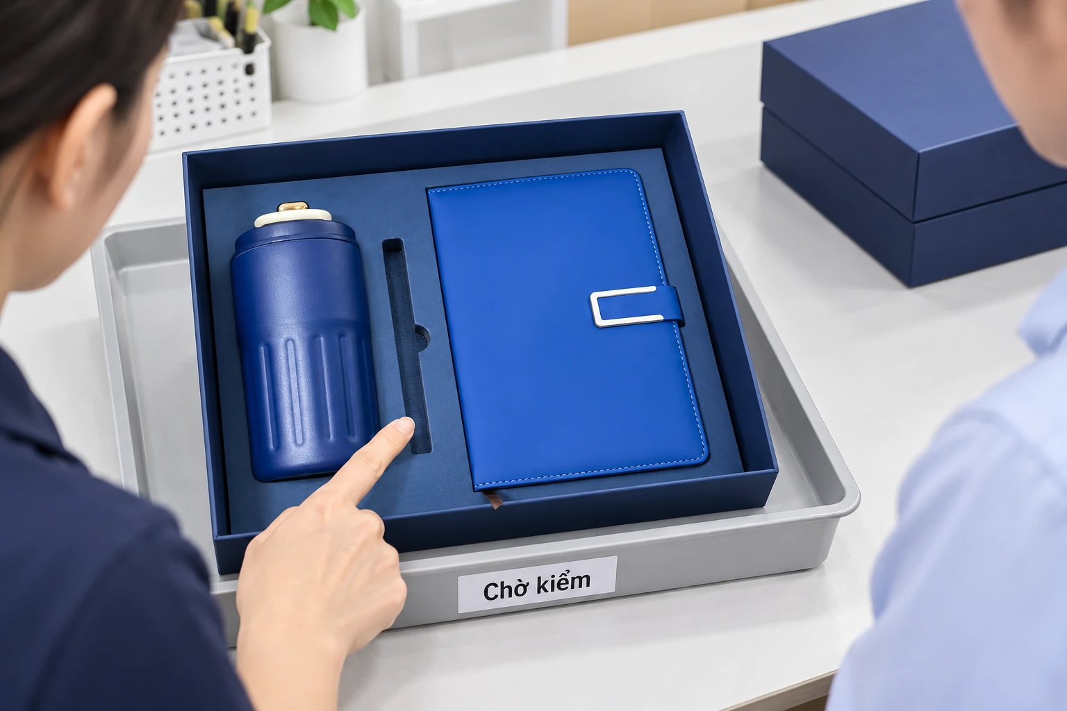 Người trực chỉ vào rãnh bút trống trong bộ quà đặt trên khay Chờ kiểm