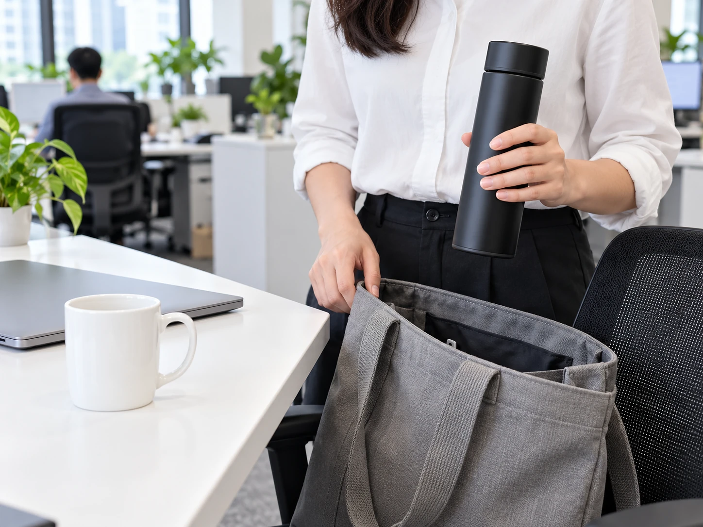 Người cầm bình đóng nắp cạnh túi đi làm, cốc trắng đặt trên bàn