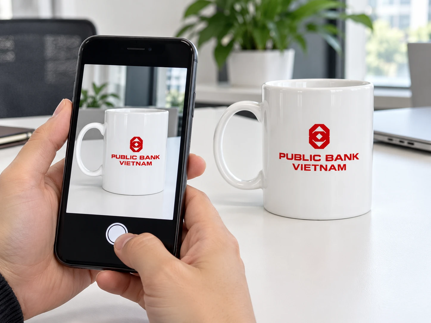 Điện thoại chụp toàn bộ cốc trắng có logo đỏ, thấy cả quai và miệng cốc
