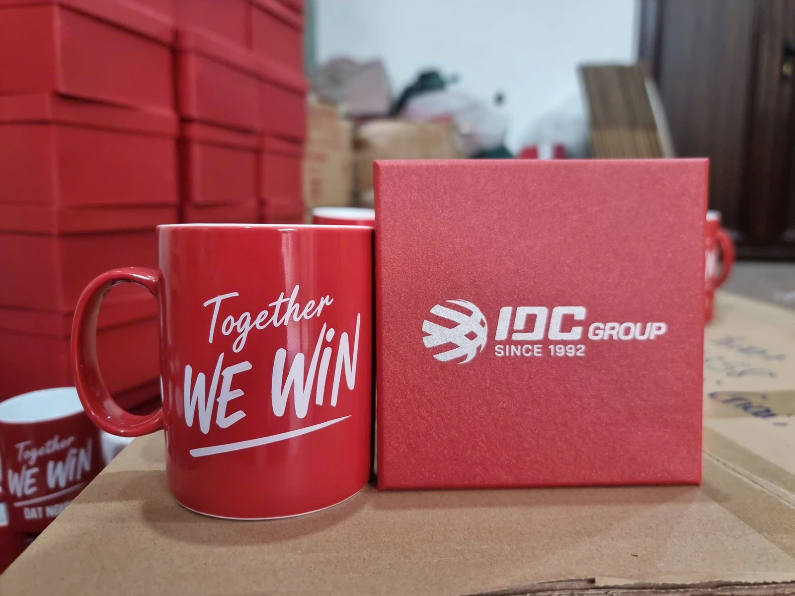 Ảnh nguồn cốc đỏ có lời nhắn Together We Win cạnh hộp mang logo IDC GROUP
