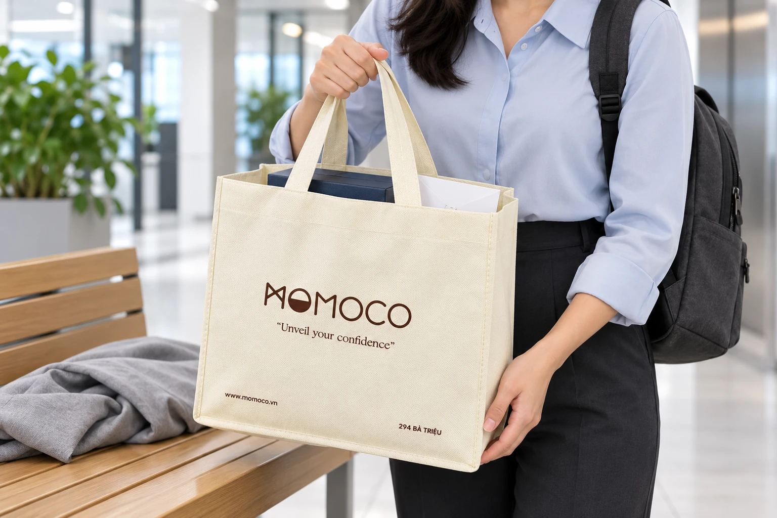 Cảnh người đeo ba lô cầm túi MOMOCO có hộp và phong bì