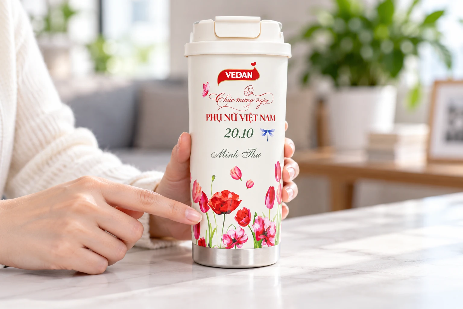 Tay chỉ vùng nền trắng sát họa tiết hoa trên bình mang logo VEDAN
