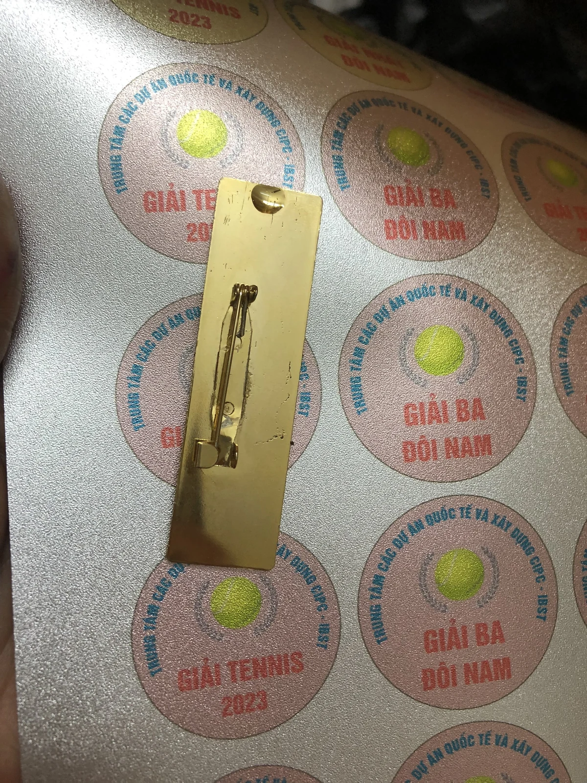 Mặt sau thẻ tên có ghim cài, đặt trên nền phôi in khác